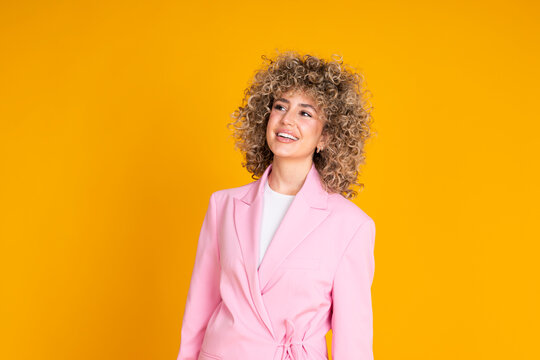 Smiling businesswoman with curly hair in a pink blazer against a yellow background