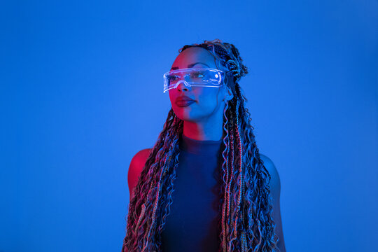 Woman with braids posing in studio wearing AR VR glasses against blue background