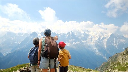 Naklejka premium Family enjoying mountain hiking, woman pointing towards the vast snowy alps peaks, children exploring nature during a summer adventure trip with scenic views