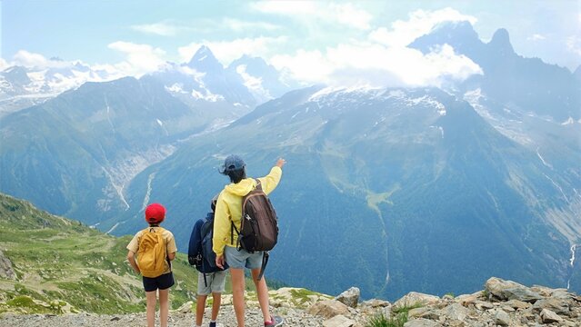 Family enjoying mountain view during summer hiking trip. Parents and children exploring french alps panorama. Pointing at distant snow-capped peaks and valleys