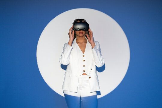 Woman with braids in white blazer posing with VR glasses in studio