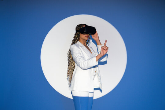 Woman in white blazer with VR glasses interacting in studio spotlight