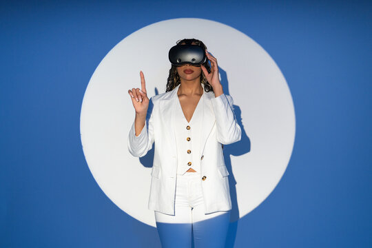 Woman in white blazer interacting with VR glasses in studio spotlight
