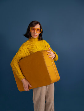Womabn with yellow suitcase and glasses in front of blue background