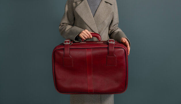 Woman in gray coat holding a vintage red leather briefcase indoors