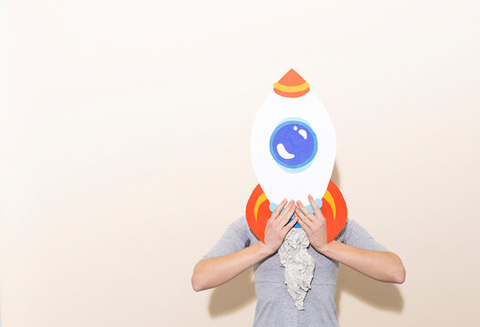 Woman with paper rocket mask representing ambition and creativity