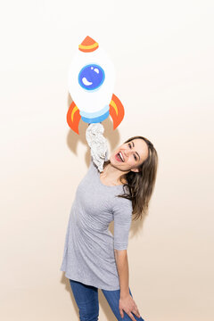 Woman in gray dress holding handmade paper rocket celebrating success