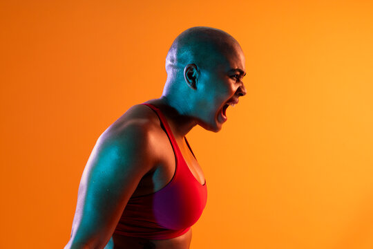 Bald athlete in sportswear screaming with motivation against orange background
