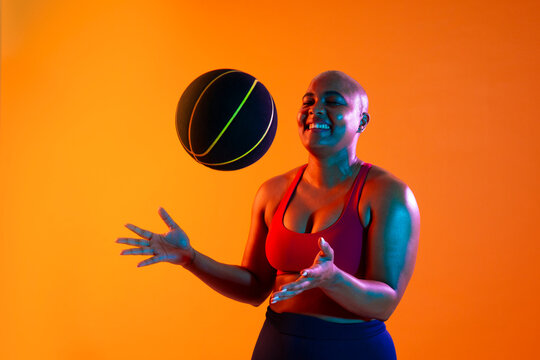 Athlete in sportswear smiling while playing with a basketball indoors