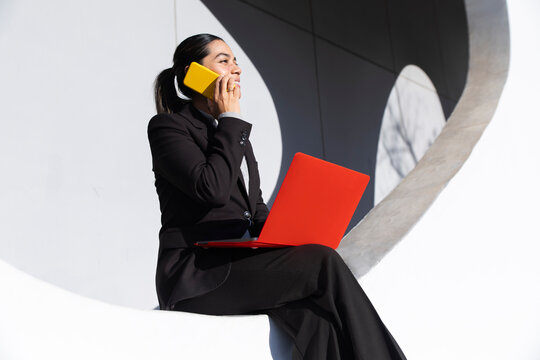 Businesswoman multitasking with smartphone and red laptop in Barcelona