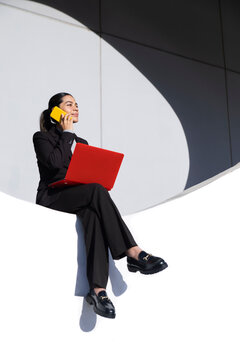 Businesswoman multitasking with smartphone and red laptop outdoors