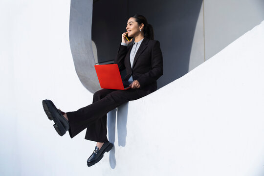 Businesswoman multitasking with smartphone and red laptop indoors