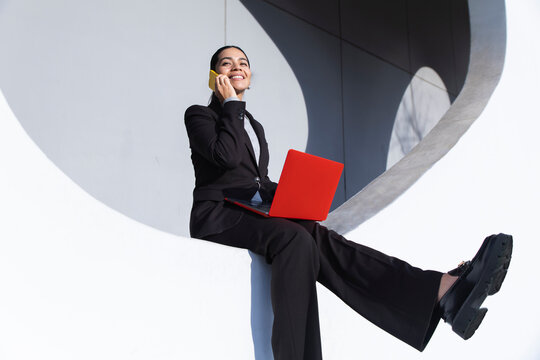 Businesswoman multitasking with red laptop and smartphone outdoors