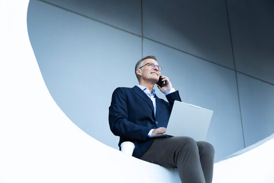 Smiling business professional multitasking with laptop and phone outdoors
