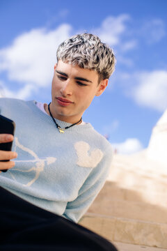 Young man sitting on outdoor steps using smartphone on a sunny day