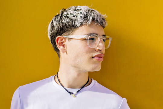 Stylish young man with glasses in white t shirt against yellow background