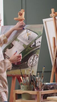A woman artist puts undone painting on an easel and continue drawing