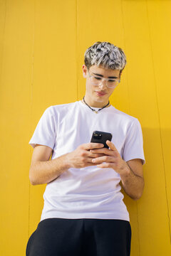Young casual man texting on smartphone against yellow wall