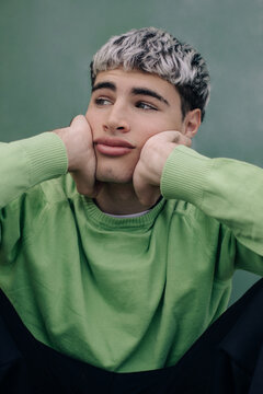 Close up of thoughtful portrait of young man with dreamy expression on green background