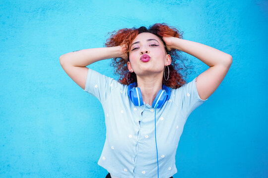 Fashionable redhead with headphones posing playfully against blue wall