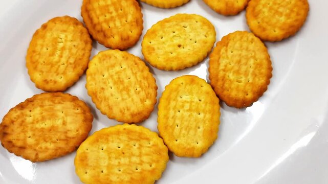 Golden brown oval crackers with textured surface appear arranged on a clean white plate, creating delightful motion footage of these delicious snacks perfect for parties or a simple savory treat.