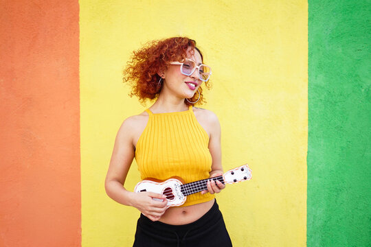 Redhead with glasses playing ukulele in yellow summer outdoor scene
