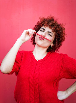 Redhead with curly hair playfully holding pencil as mustache