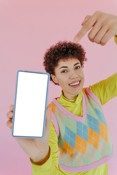 Smiling woman presenting phone with blank screen on pink background