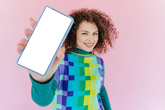 Smiling woman holding smartphone with blank screen on pink background