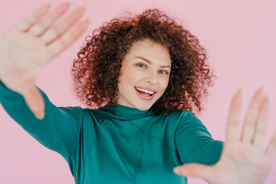 Smiling woman gesturing frame playfully in front of pink background