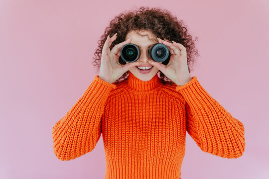 Smiling woman with curly hair holding lenses in front of eyes indoors