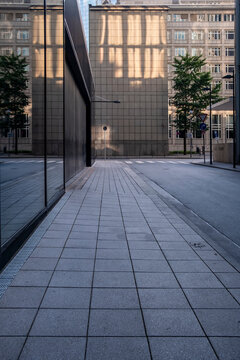Empty urban plaza with glass reflection and modern architecture symmetry on clean pavement with trees creating a corporate public space concept