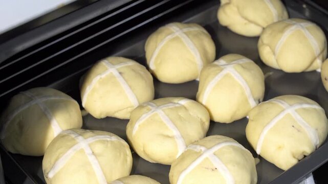 The appetizing and glossy Easter hot cross buns are about to be baked &mdash; the raw buns are carefully placed into the preheated oven, ready to transform into warm, fragrant treats. Meanwhile, the cozy at