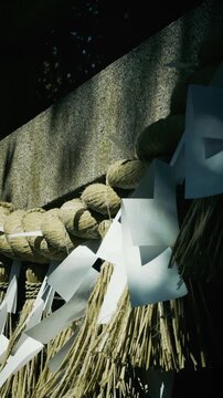 Close-up of Sacred Shimenawa Rope and Shide Paper Streamers on Stone at Japanese Shrine, Vertical