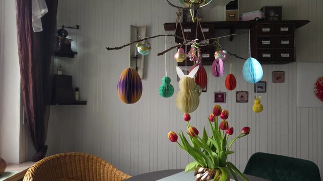 Easter idea inspiration: a hanging Easter bouquet. Honeycomb paper bunnies and eggs in pastel shades, as well as vintage glass figurines. Fresh red and yellow tulips are in the foreground.
