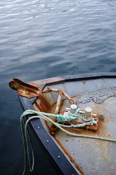 The prow of a steel hulled boat with an anchor attached to rope and chain on board sitting in a calm sea