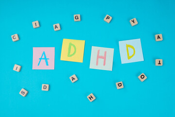Colorful Sticky Notes Spelling ADHD Surrounded By Scattered Wooden Letter Tiles On Blue Background