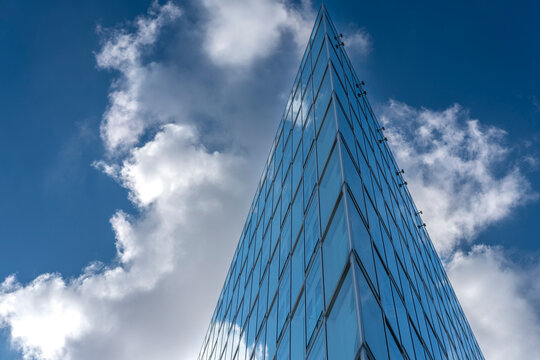 Glass skyscraper tower in modern urban architecture from upward view with reflective facade under sky and cloud creating clean geometry lines for background