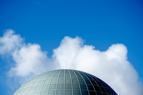 Glass dome with modern curved architecture as an urban landmark beneath daylight sky and sculpted cloud creating clean background space for contemporary design