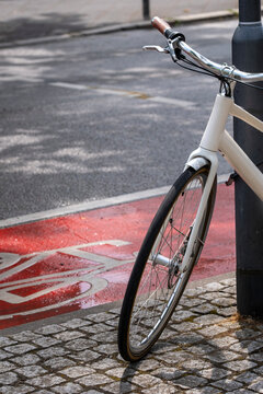 Closeup detail of a parked bicycle wheel by curb on an urban street lane showing transportation texture and city commute atmosphere