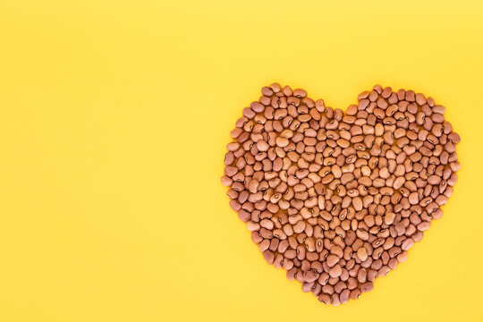 Organic Red beans in a shape of heart on yellow background. Top view