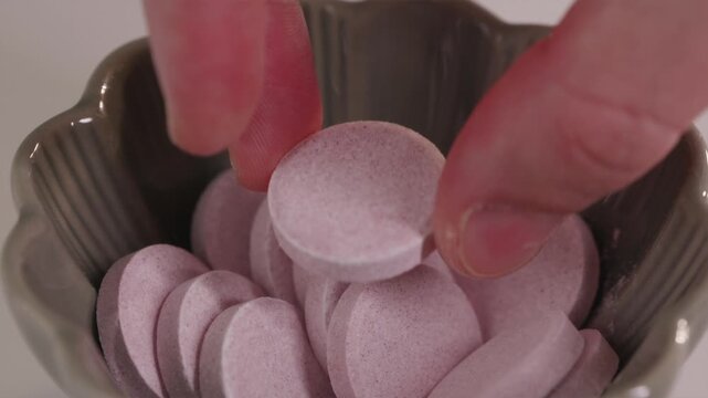 Detailed shot of fingers taking a red round pill from a bowl