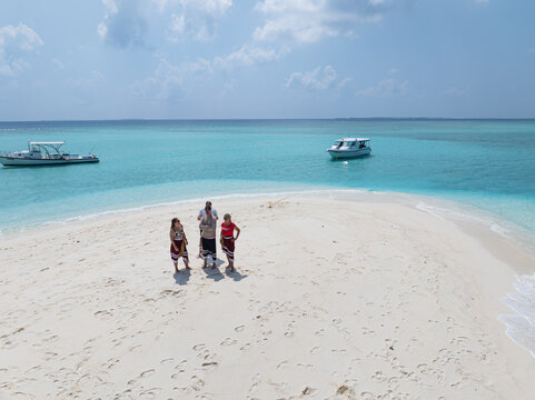 Aerial view of three people standing on white sand meeting point while boats float on turquoise water, Dhidhdhoo, Thiladhunmathee Uthuruburi, Maldives.