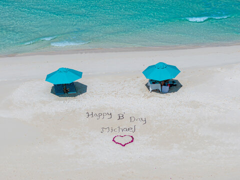 Aerial view of turquoise umbrellas casting shadows on the pristine white sands where a birthday message is written, Dhidhdhoo, Thiladhunmathee Uthuruburi, Maldives.