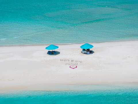 Aerial view of turquoise waters meet the pristine white sands, adorned with sunshades and a heartfelt message, Dhidhdhoo, Maldives.
