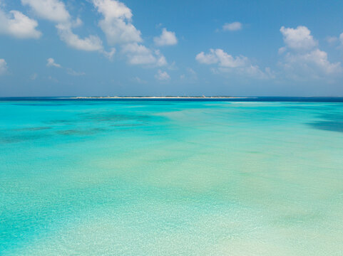 Aerial view of turquoise waters meeting the horizon under a bright sky spotted with fluffy clouds, Dhidhdhoo, Thiladhunmathee Uthuruburi, Maldives.