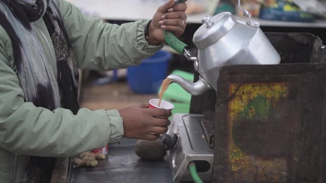 Street tea vendor pouring chai, Indian chaiwala serving tea close up, Hot tea being poured from kettle, Roadside tea stall serving chai stock video.