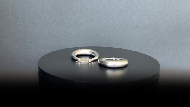 Pendientes de aro plateados girando 360 grados sobre base negra