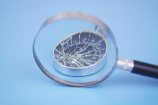Broken compass under magnifying glass on blue background.	