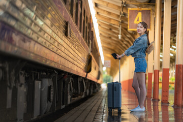 Young woman traveler with suitcase waiting at train station platform, travel and transportation...